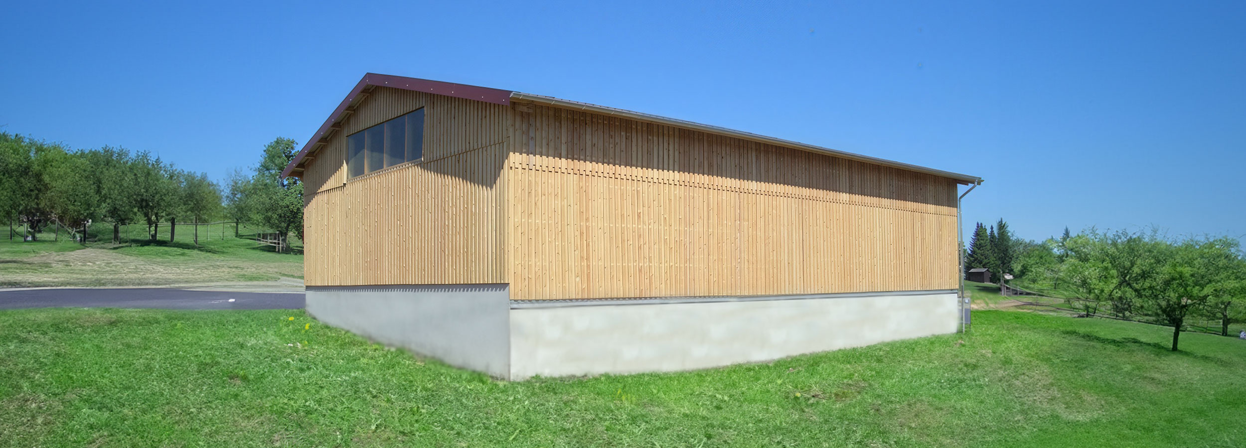 Neue Holzhalle mit Holzverschalung auf grüner Wiese unter blauem Himmel