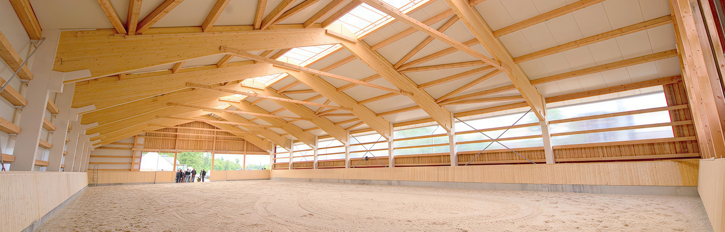 Innenraum einer hellen Reithalle mit Holzbinder-Konstruktion